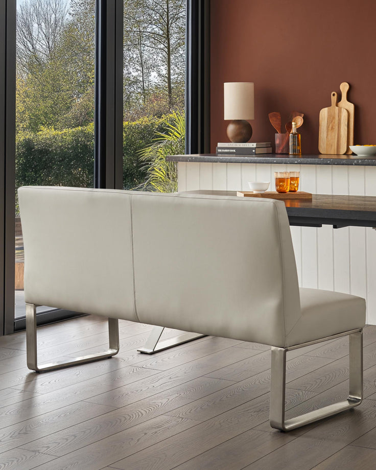 A contemporary dining bench with grey leather upholstery and stylish stainless steel legs.