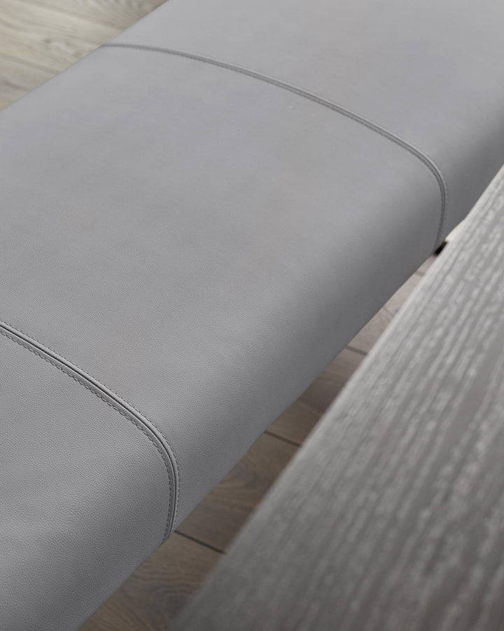 Close-up of a grey upholstered bench seat with stylish stitching detail, sitting on a wooden floor.