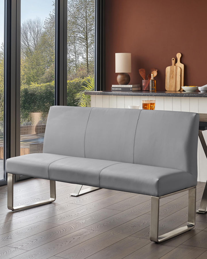 A grey bench with a stainless steel base sits in front of a window in a modern kitchen.