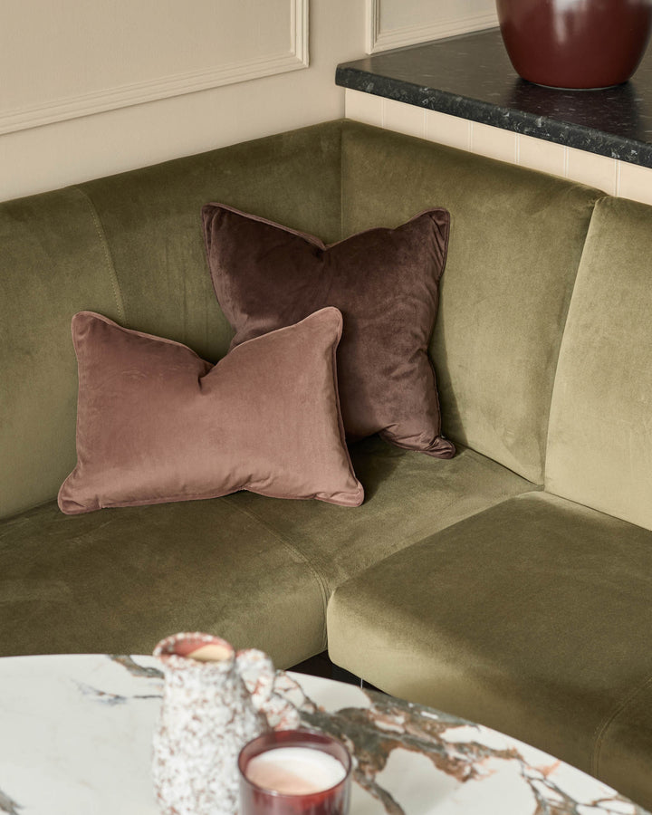 Olive green velvet corner bench with mauve and burgundy cushions, black marble countertop, and cream paneled wall backdrop.