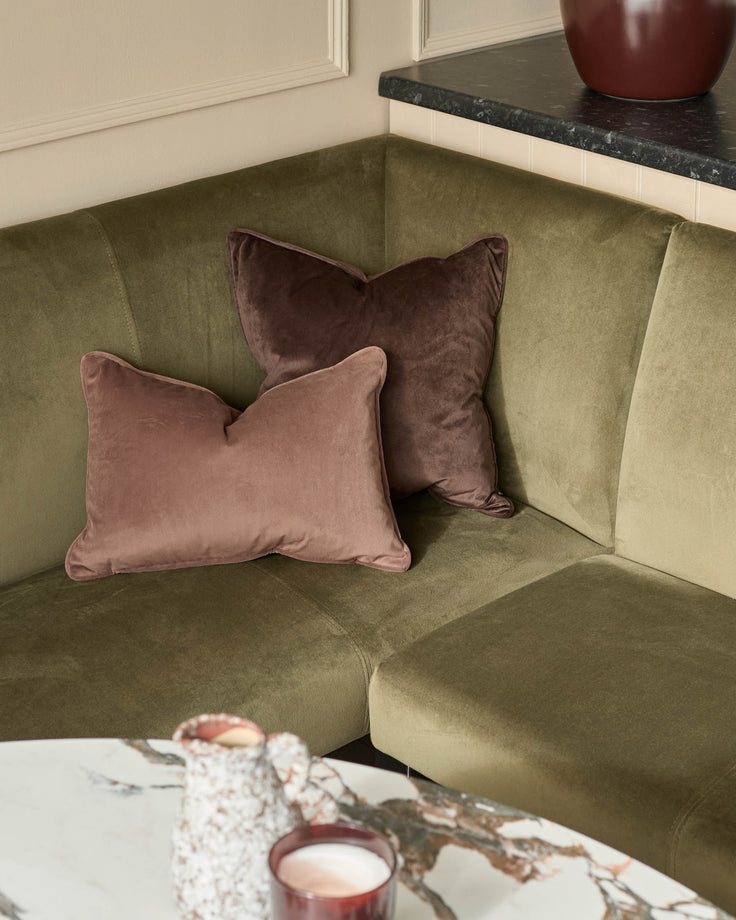 Olive green velvet corner bench with mauve and burgundy cushions, black marble countertop, and cream paneled wall backdrop.