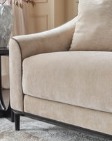 Champagne fabric 3-seater sofa with curved arms, black wooden legs, and matching throw pillow detail.