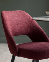 Close-up of a stylish, textured maroon chair with sleek black legs, set against a muted green wall.