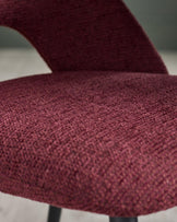 Close-up of a stylish chair with a textured, deep red fabric and a curved backrest. Modern and comfortable design.