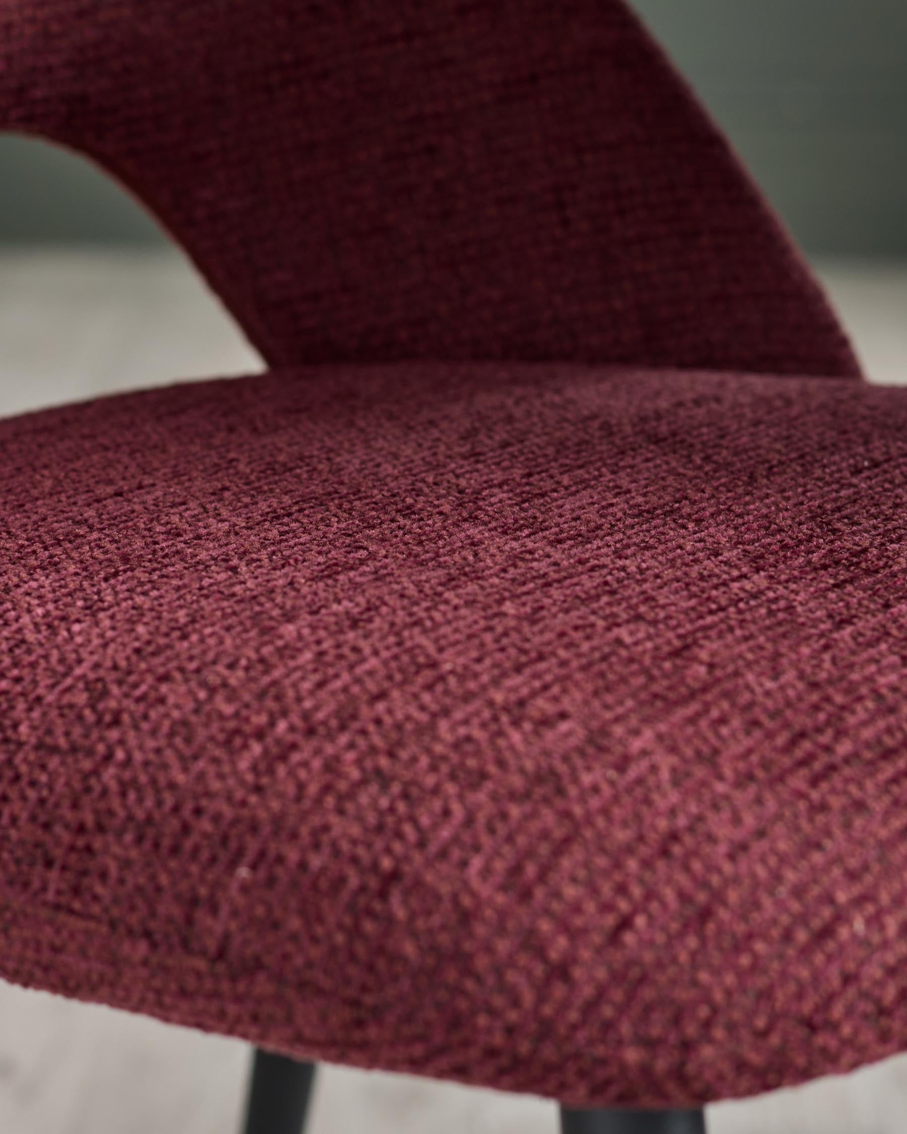 Close-up of a stylish chair with a textured, deep red fabric and a curved backrest. Modern and comfortable design.