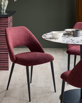Stylish dining setting with modern chairs upholstered in a textured, deep red fabric and sleek black legs, around a marble-effect table.