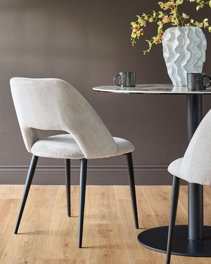 Lottie fabric dining chair in mid-grey with curved backrest and black legs, shown at round table with decorative vase.