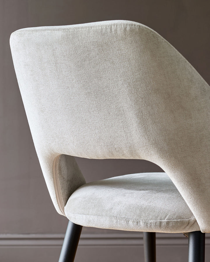 Lottie fabric dining chair in cream, angled side view showing curved backrest and dark wooden legs.