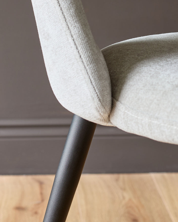 Lottie fabric dining chair in light grey, close-up of curved armrest and dark metal leg detail.