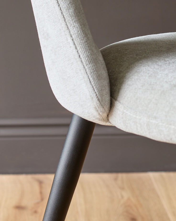Lottie fabric dining chair in light grey, close-up of curved armrest and dark metal leg detail.