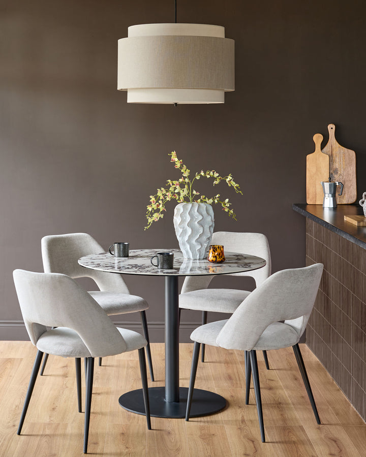 Lottie fabric dining chair in mid-grey, shown in a styled dining setting with curved backrest and black tapered legs.