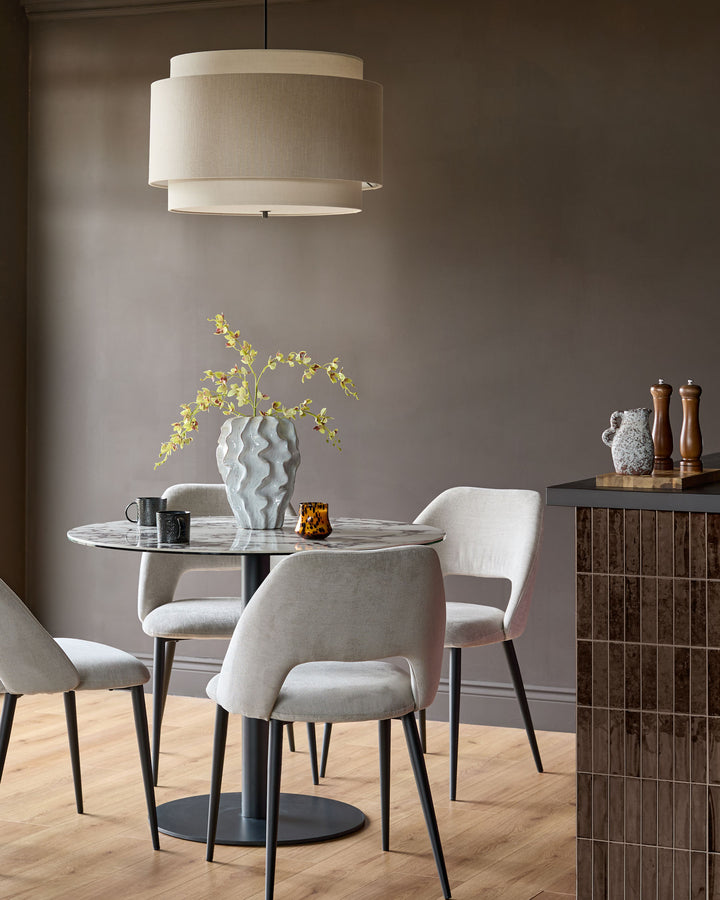 Lottie mid-grey fabric dining chair with curved backrest and dark tapered legs, shown at round marble table.