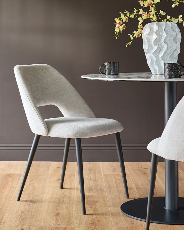 Lottie fabric dining chair in mid-grey with black metal legs, shown at a round table with marble top and decorative vase.