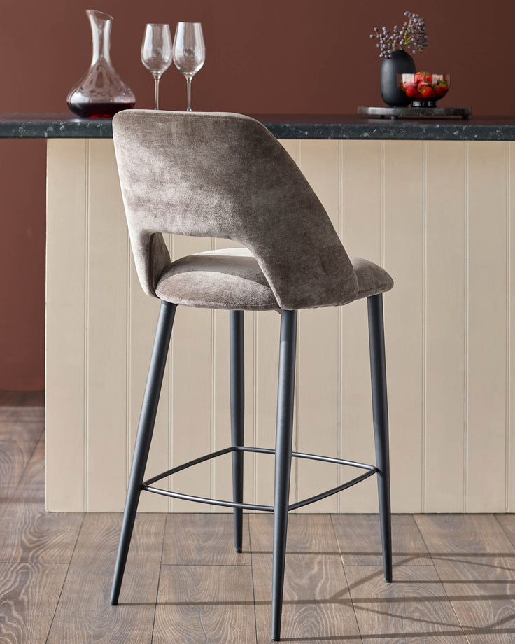 Upholstered bar stool in mink velvet with black metal legs, positioned in front of a kitchen island.