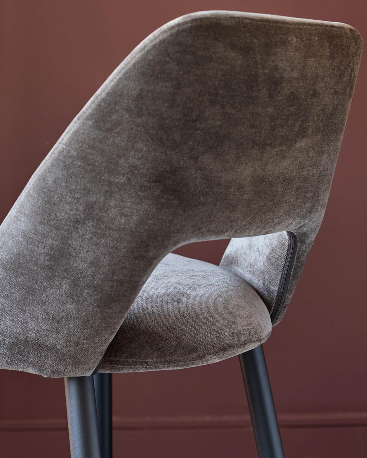 Close-up of a brown velvet chair with black legs against a red wall, showcasing its stylish design and luxurious material.