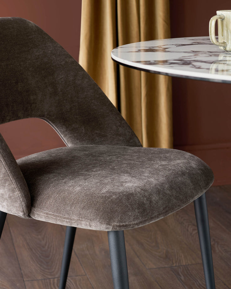 A stylish dining area with a brown velvet chair and marble table, complemented by warm curtains.