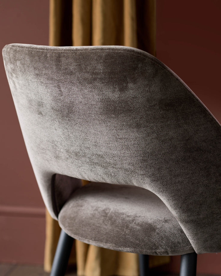 Close-up of a stylish, brown velvet chair with a curved backrest and sleek black legs. Modern design for sophisticated interiors.
