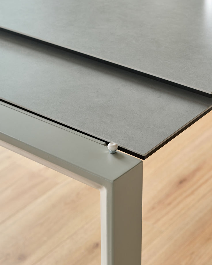 Close-up of Louis ceramic extending dining table leg and top edge, showing grey ceramic surface with white metal frame detail.