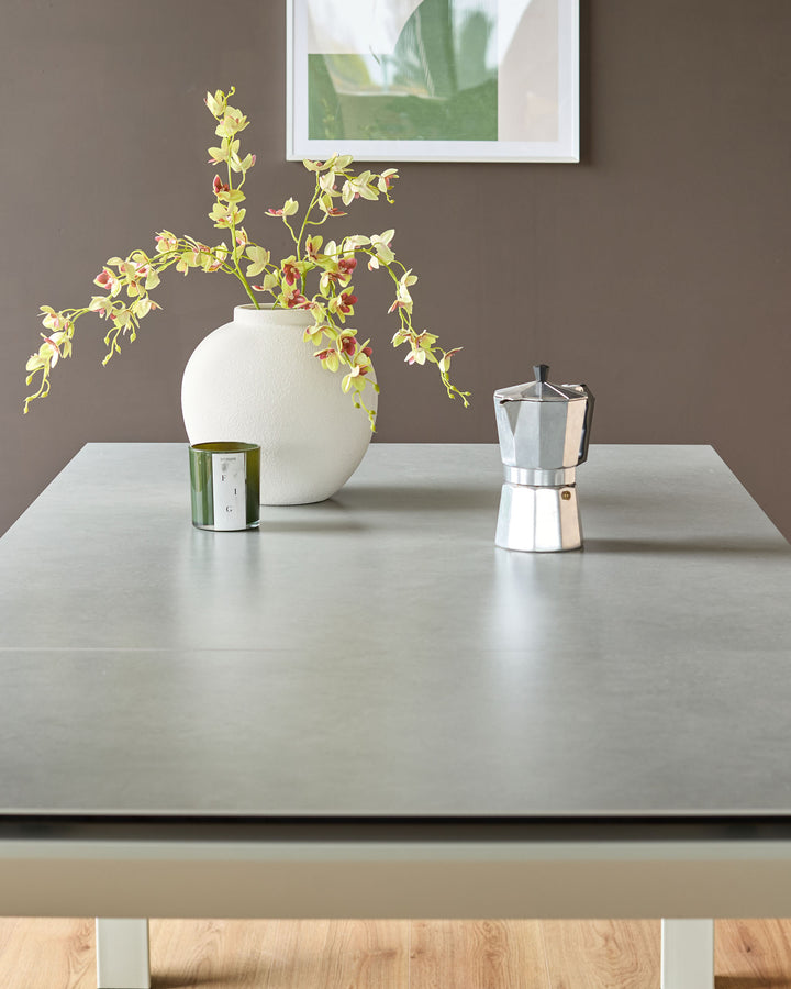 Light grey ceramic extending dining table with wooden base, styled with white vase, candle, and coffee maker.