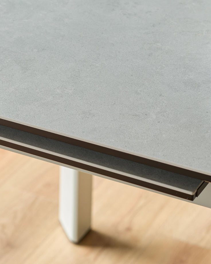 Light grey ceramic extending dining table with dark metal handle detail and white pedestal base, angled close-up view.