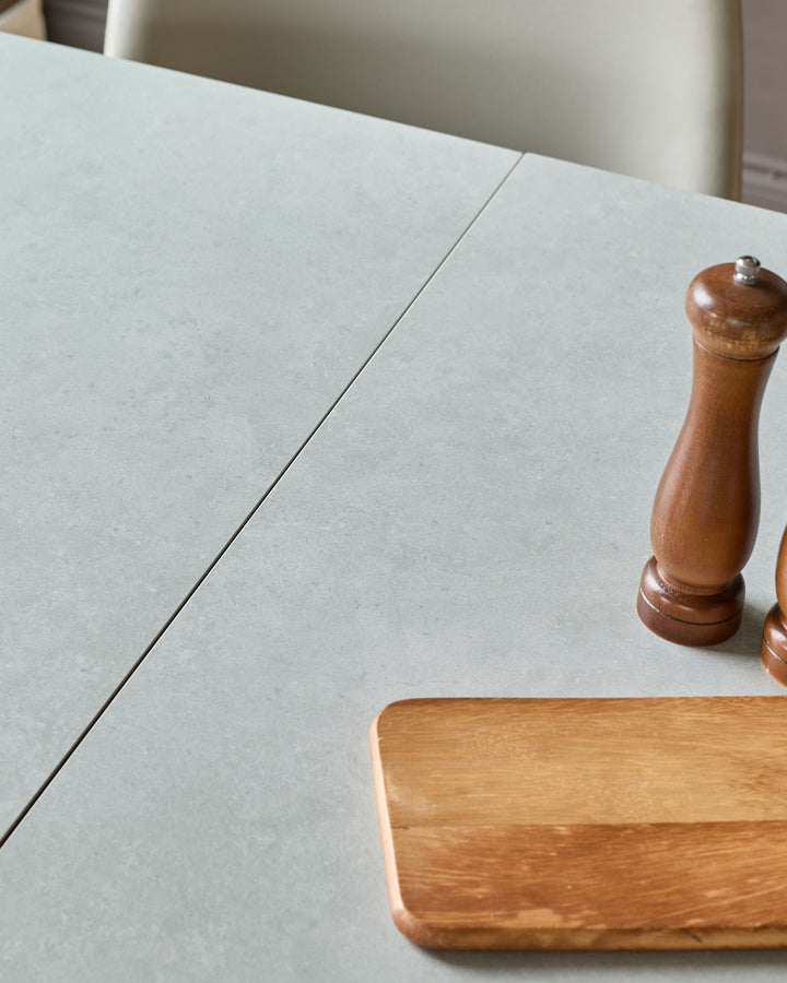 Light grey ceramic extending dining table with central seam, styled with wooden pepper mill and cutting board.