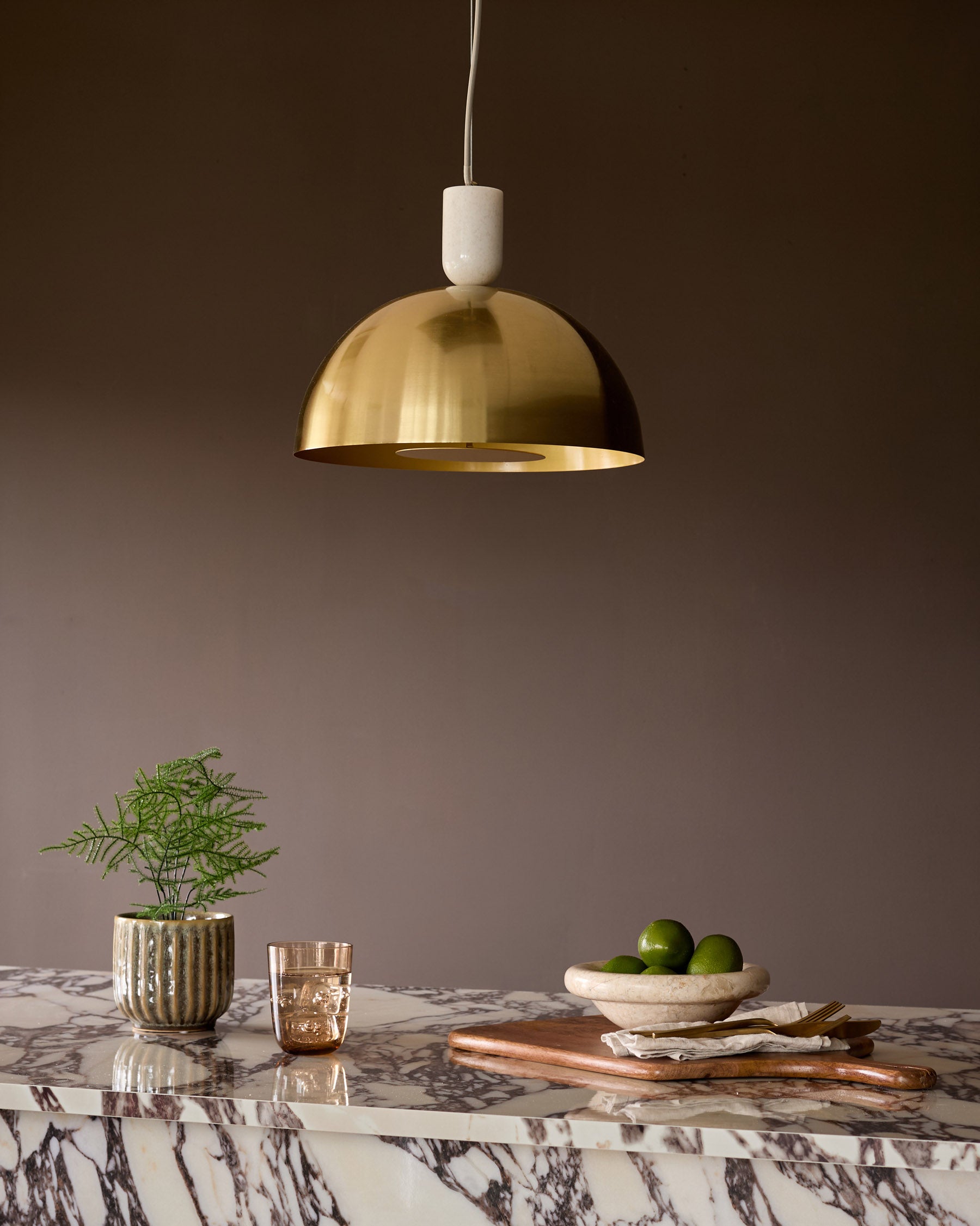 Louis single pendant brass light hanging above a marble table with interior styling.