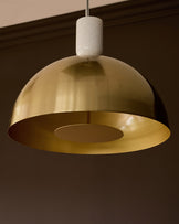 Louis single pendant brass light with white ceramic canopy, suspended against dark ceiling background.