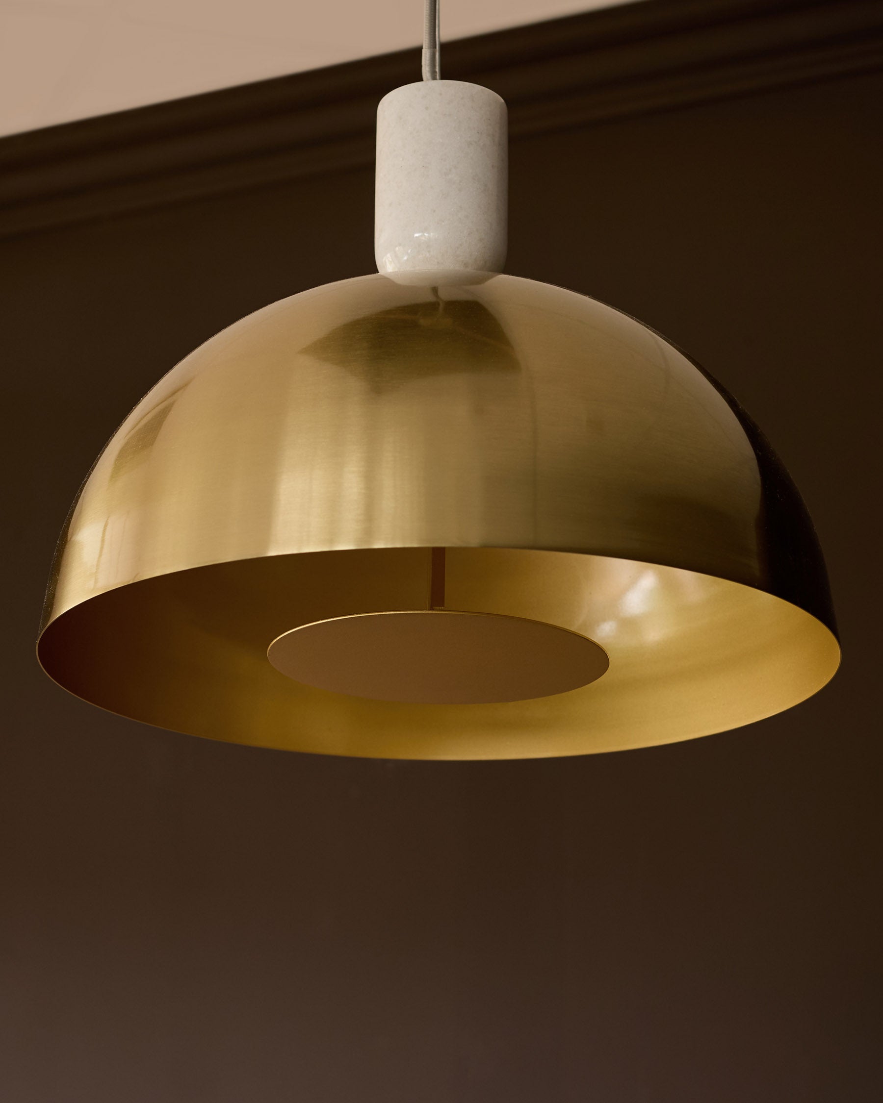 Louis single pendant brass light with white ceramic canopy, suspended against dark ceiling background.