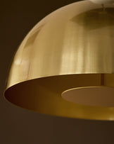 Louis single pendant brass, dome-shaped shade with warm brass finish, angled side view showing curved form and interior reflections.