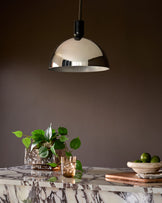 Chrome dome pendant light hanging above marble countertop with plants and fruit bowl.
