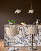 Chrome dome pendant light hanging above a marble dining table with cream chairs.