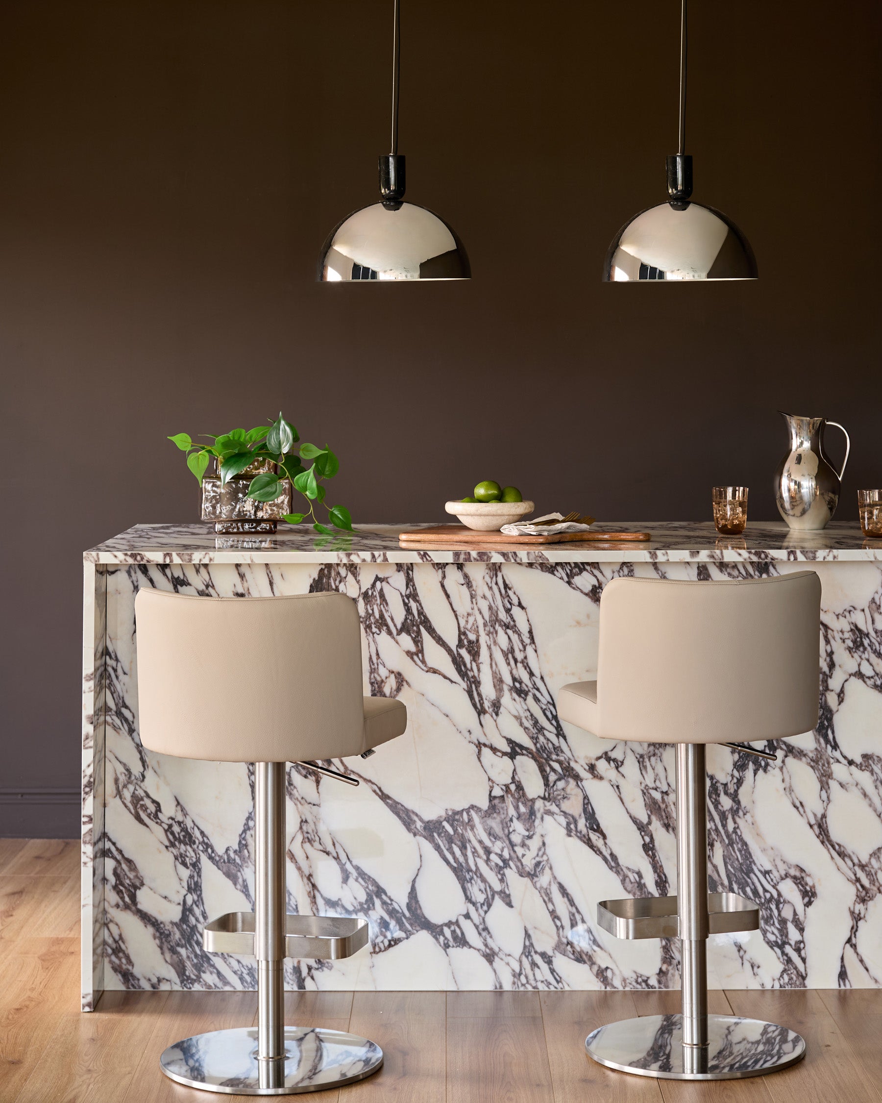 Chrome dome pendant light hanging above a marble dining table with cream chairs.