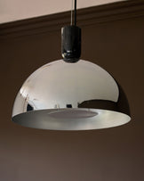 Chrome dome pendant light with black cylindrical canopy and frosted glass diffuser, suspended against neutral wall.