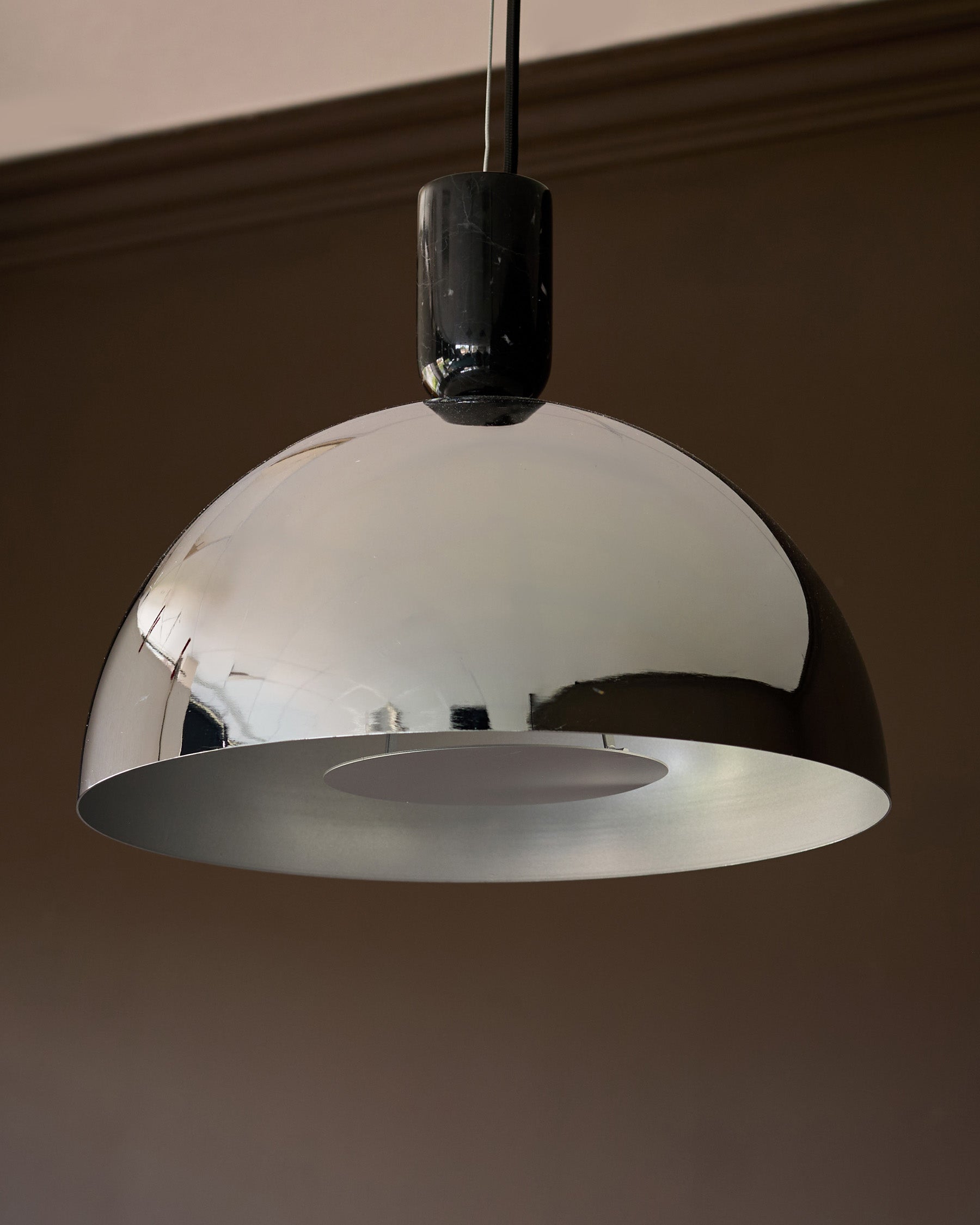 Chrome dome pendant light with black cylindrical canopy and frosted glass diffuser, suspended against neutral wall.