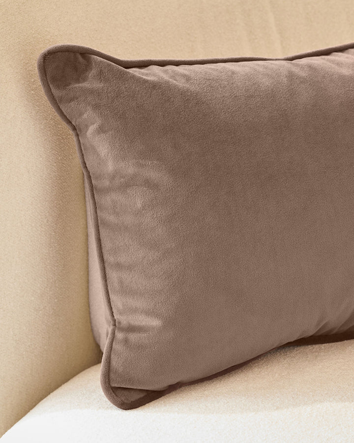 Luca rectangle cushion in mink velvet, displayed on a neutral cream sofa showing its soft texture and piping detail.