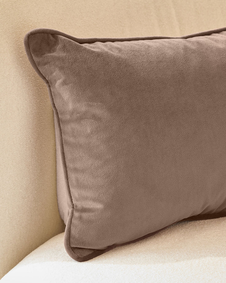 Luca rectangle cushion in mink velvet, displayed on a neutral cream sofa showing its soft texture and piping detail.