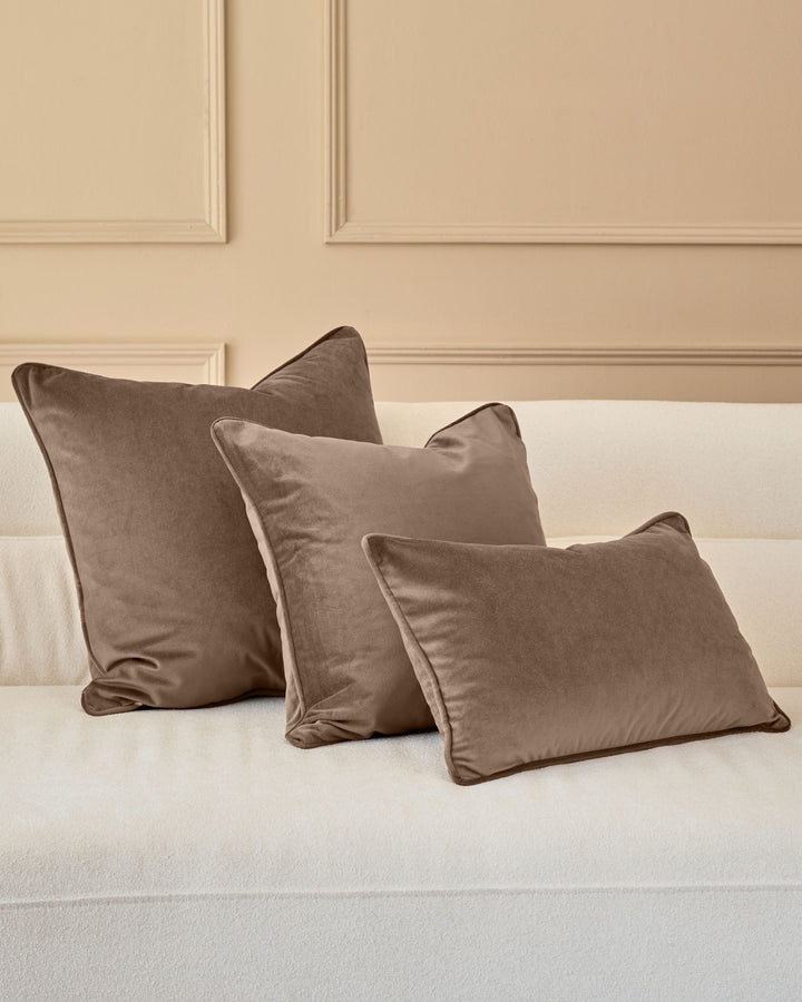 Luca Rectangle Cushion in Mink displayed on a cream sofa against a beige panelled wall.