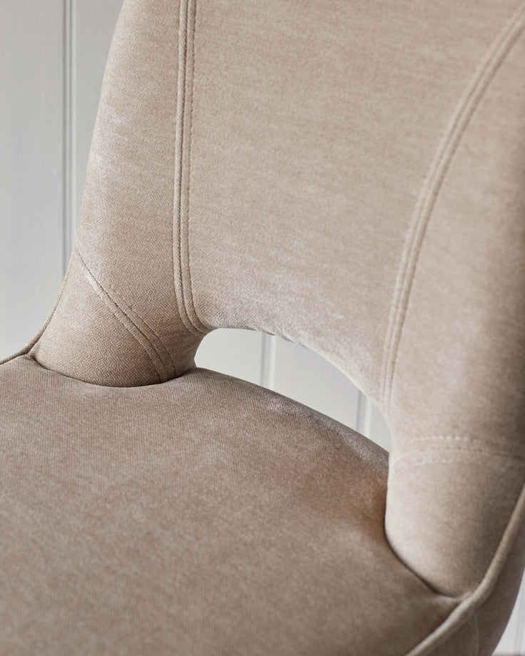 Close-up of a stylish upholstered chair in a neutral tone with detailed stitching, part of a modern furniture collection.