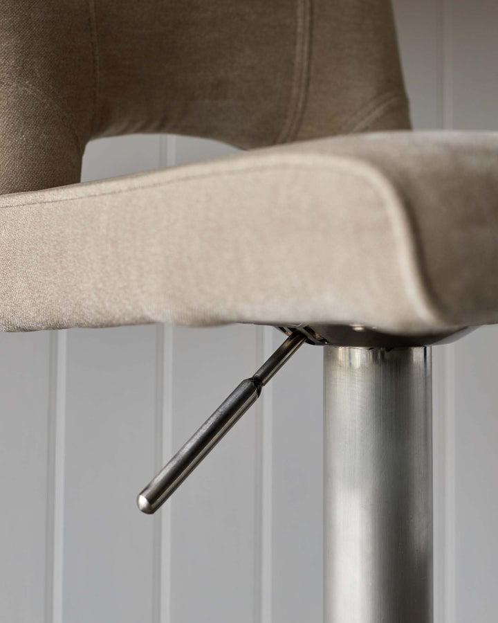 Close-up of an adjustable bar stool featuring a brushed metal base and beige upholstered seat.