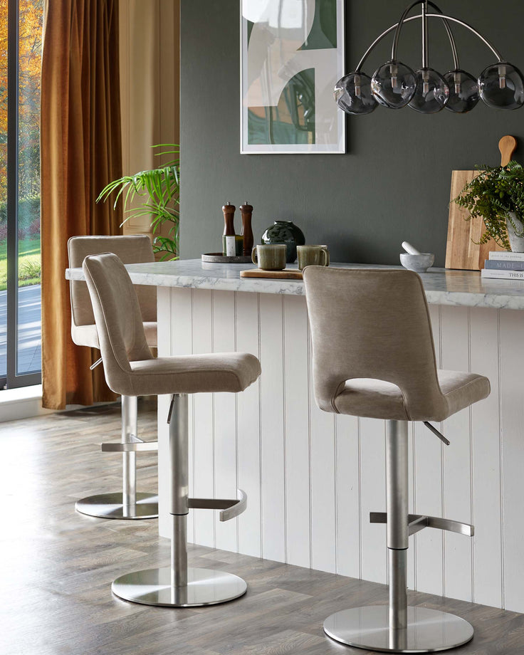 Three kitchen bar stools with neutral upholstery and brushed steel legs, lined up at a marble countertop breakfast bar.