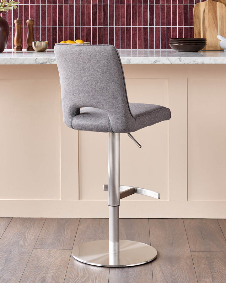 Dark grey fabric gas lift bar stool with brushed metal pedestal base and footrest, shown in kitchen setting.
