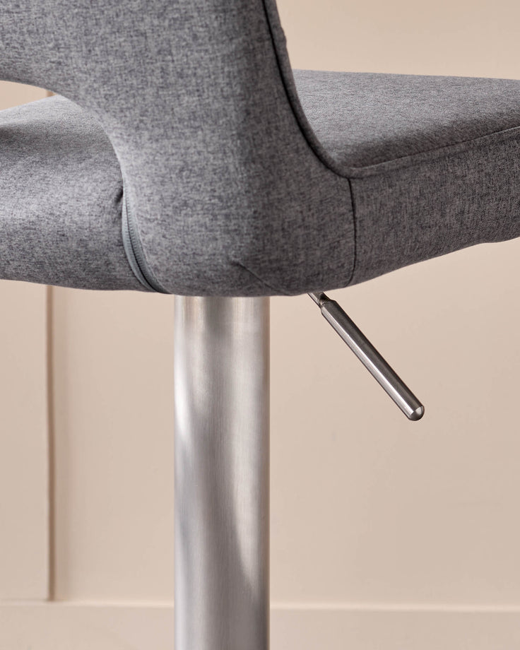 Dark grey fabric gas-lift bar stool with brushed metal pedestal base and hydraulic adjustment lever, side detail view.