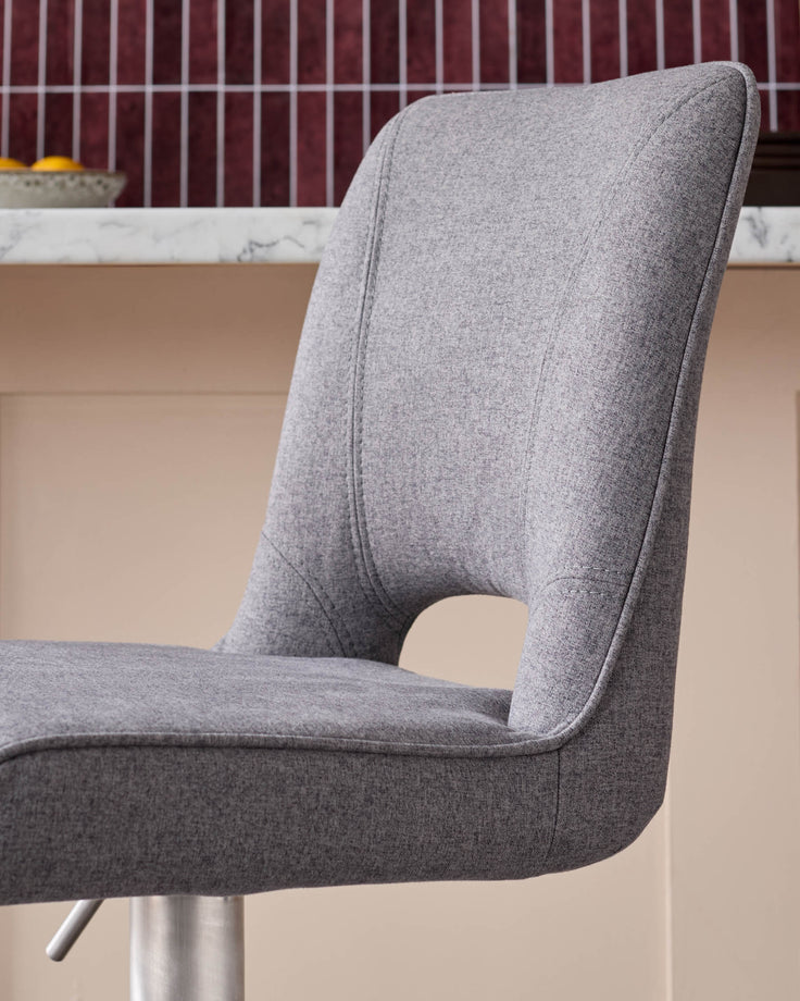 Grey fabric gas lift bar stool with curved backrest and chrome base, side angle view.