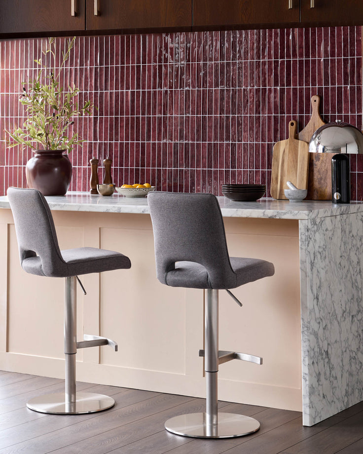 Dark grey fabric gas lift bar stools with brushed metal bases, shown at a marble kitchen island.