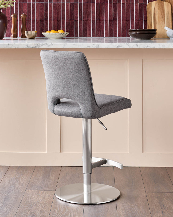 Dark grey fabric gas lift bar stool with brushed metal base and footrest, shown in kitchen setting.