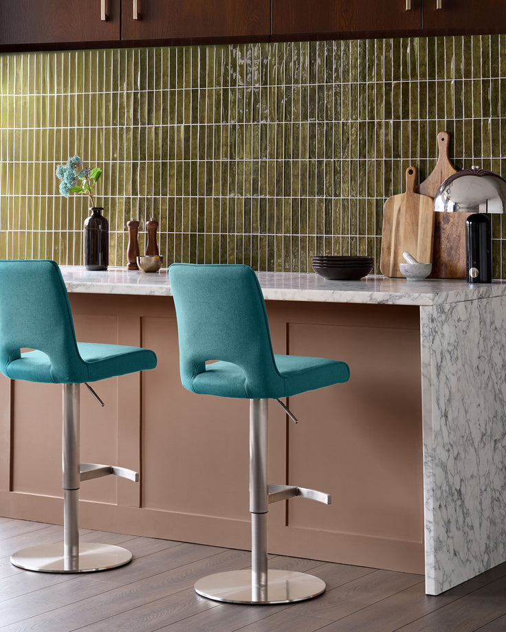 Light teal fabric gas-lift bar stool with chrome base, shown at kitchen island with marble countertop and green tile backsplash.
