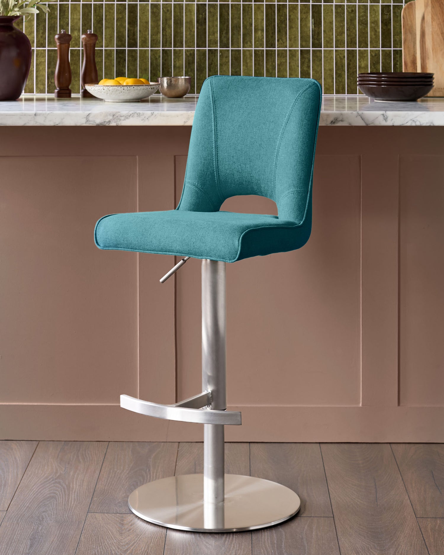 Light teal upholstered bar stool with curved backrest, chrome gas-lift mechanism, footrest, and round brushed metal base.
