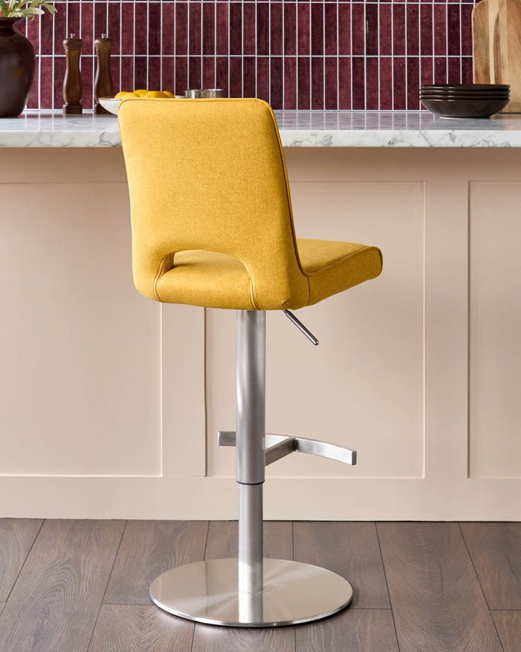 Mustard yellow fabric gas lift bar stool with curved backrest and chrome pedestal base in modern kitchen setting.