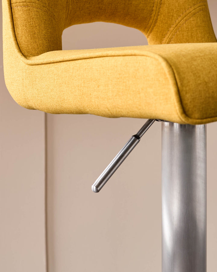 Mustard yellow fabric bar stool with curved backrest and armrests, featuring a brushed metal gas lift pedestal base.