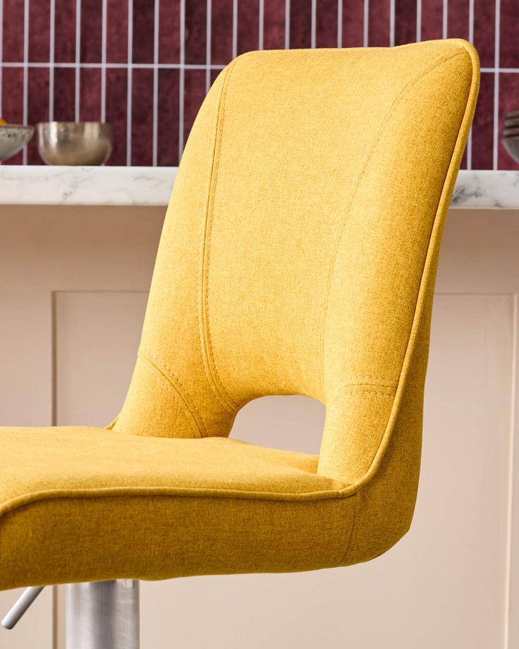 Mustard yellow fabric gas lift bar stool with curved backrest and metal base, side view.